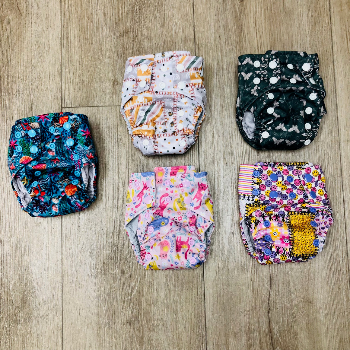 Stack of colorful patterned cloth diapers on a wooden floor, Texas Tushies