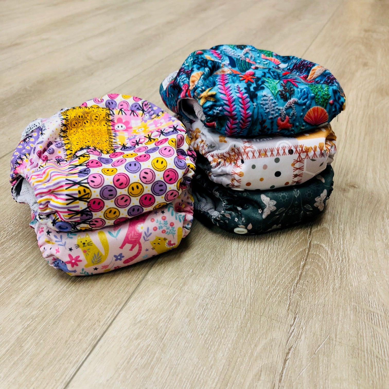 Stack of colorful patterned cloth diapers on a wooden floor, Texas Tushies