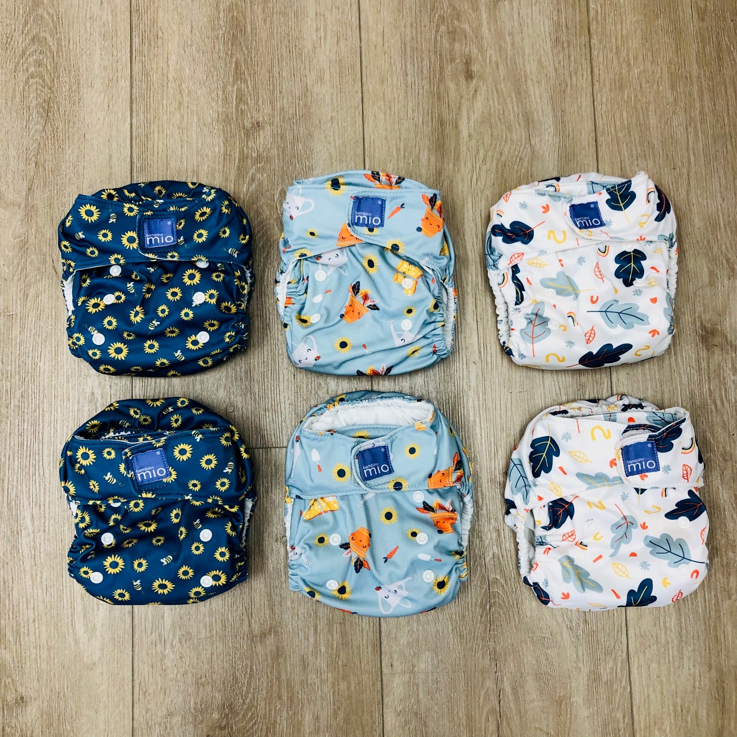Set of six patterned Bambino Mio cloth diapers on a wooden surface