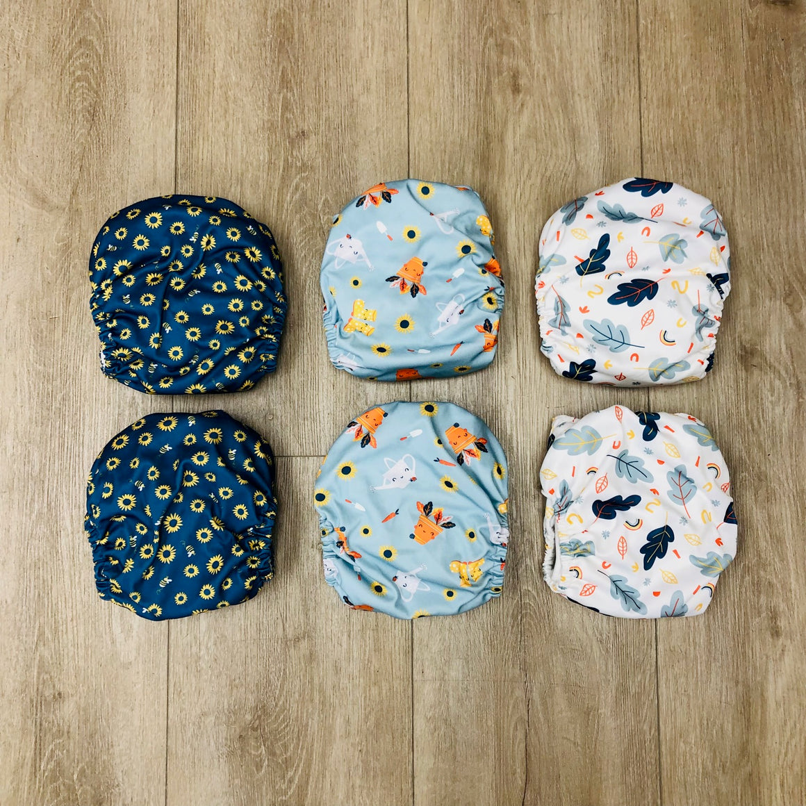 Set of six patterned Bambino Mio cloth diapers on a wooden surface