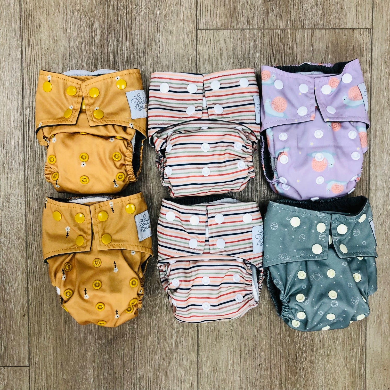 Set of patterned La Petite Ourse newborn cloth diapers on a wooden surface