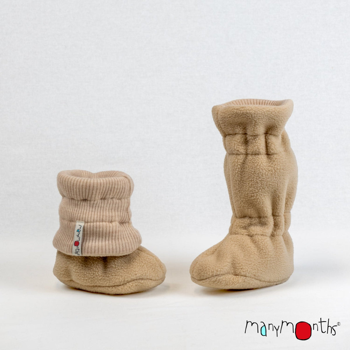 A pair of callisto moon brown fleece baby booties with ribbed knit wool cuffs, shown on a light gray background. One bootie is upright and the other is folded down, showing a small white brand tag on the cuff. ManyMonths brand logo in bottom right corner