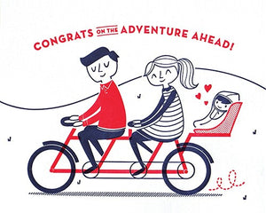 baby bicycle good paper greeting card features a couple riding a navy and red tandem bike with a baby seat holding a baby and the words "congrats on the adventure ahead"